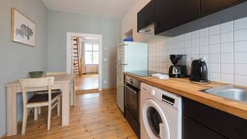 A compact kitchen with a wooden countertop, a washing machine, a coffee maker, and a refrigerator.