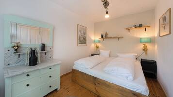 A bedroom with a bed, a nightstand, a dresser, a mirror, and wall-mounted shelves.