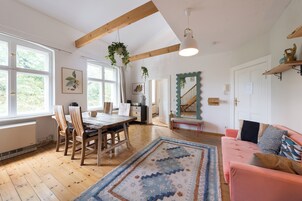 Una habitación con una mesa de comedor de madera, sillas, un sofá rosa, un tapete estampado y una escalera con un espejo decorativo.