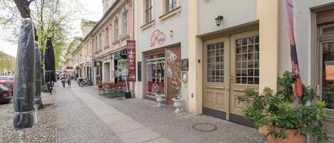A cobblestone street lined with historic buildings, including a cafe with outdoor seating and a shop with a visible sign.