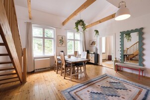 Un comedor con mobiliario de madera, ventanas amplias y plantas colgantes.
