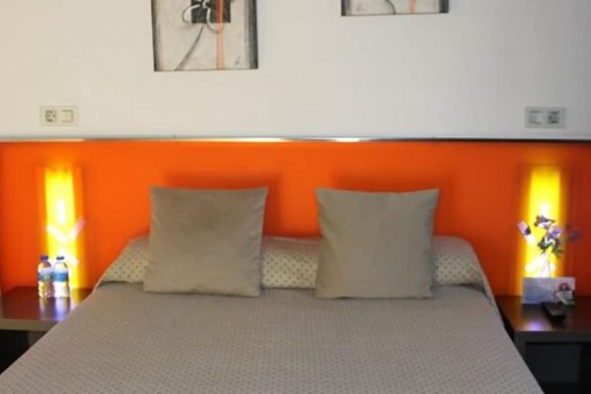 A hotel room with a bed, two nightstands, and a wall-mounted light fixture.