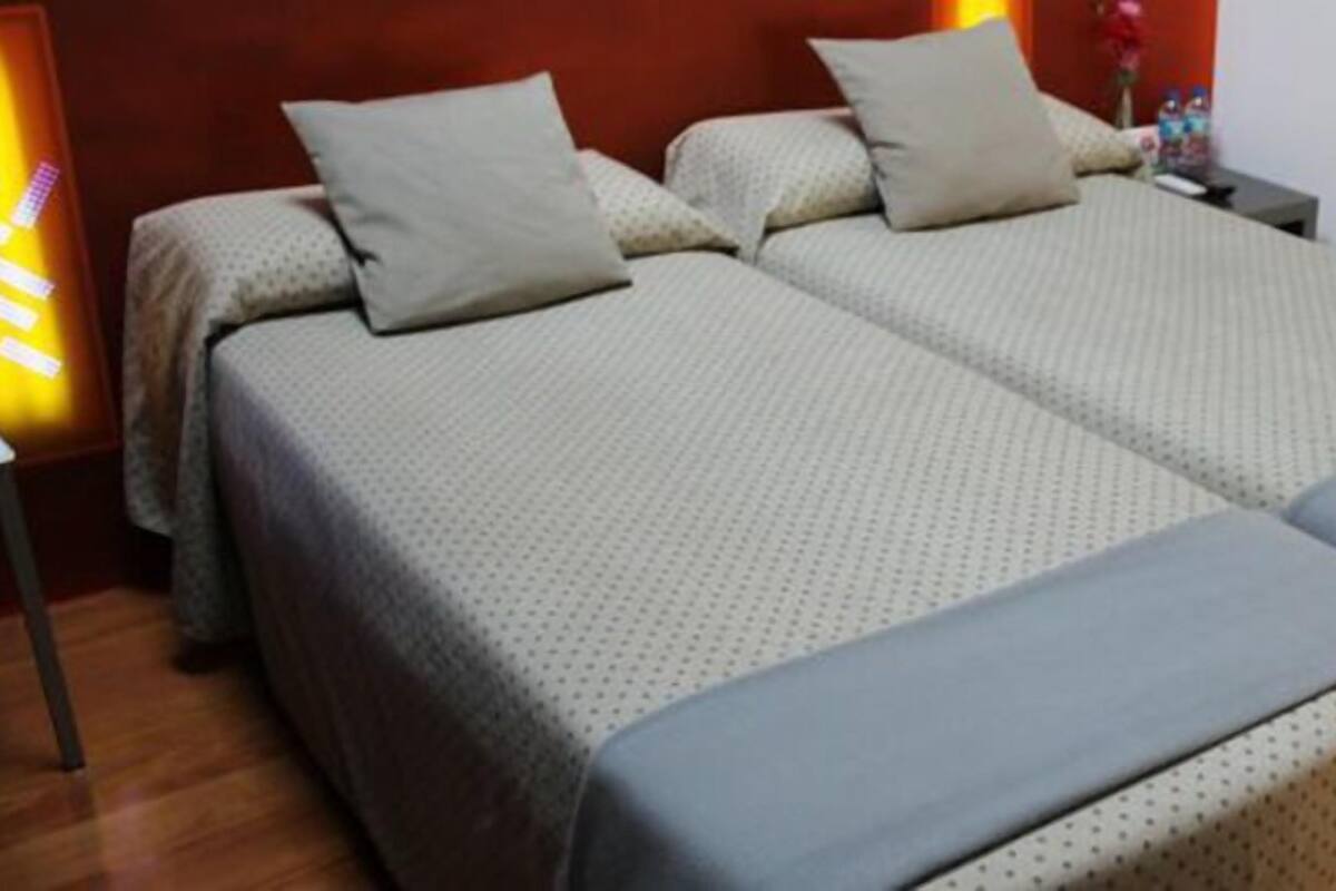 A double bed with a grey duvet and matching pillows, a wooden floor, and a nightstand with a lamp.