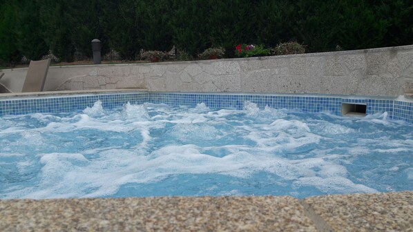 A hot tub with bubbling water, surrounded by a stone wall and greenery.