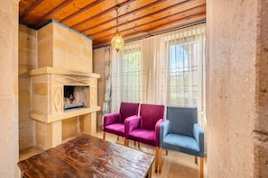 A room with a stone fireplace, wooden ceiling beams, a table, and two upholstered chairs.