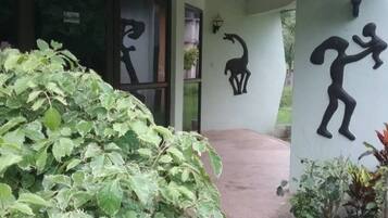 Entrada de un edificio con un camino de hormigón que lleva a una puerta, rodeada de vegetación y decoración mural.
