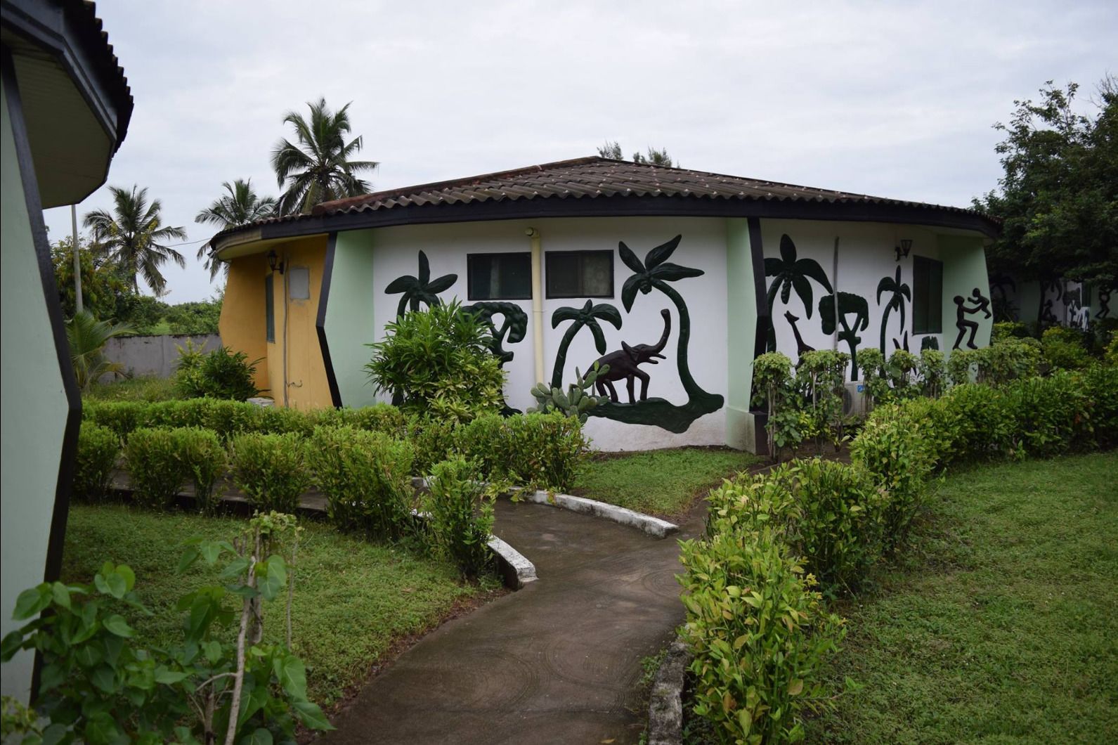 Una casa con un camino de jardín que la conduce, rodeada de follaje y palmeras.