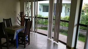Un comedor con mesa y sillas, ventanas grandes con cortinas y vistas a zonas verdes exteriores.