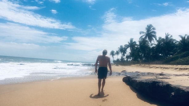 Una persona caminando sobre una playa arenosa con palmeras al fondo.