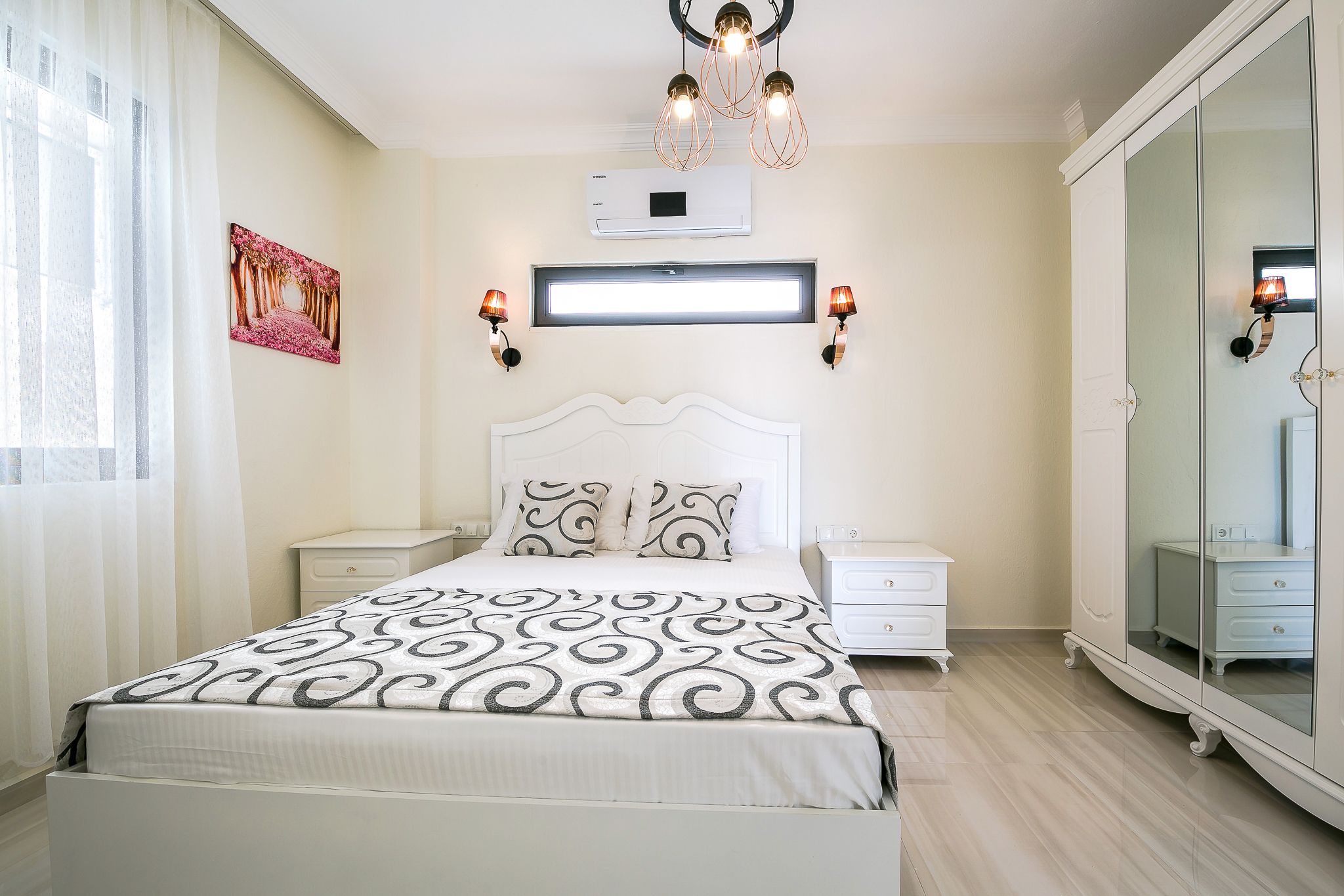 A bedroom with a bed, bedside tables, a mirror, and a ceiling light fixture.