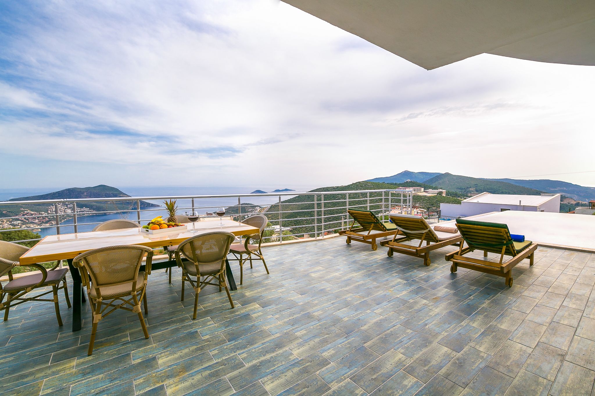 A terrace with a table and chairs, overlooking a coastal view with mountains and a city in the distance.