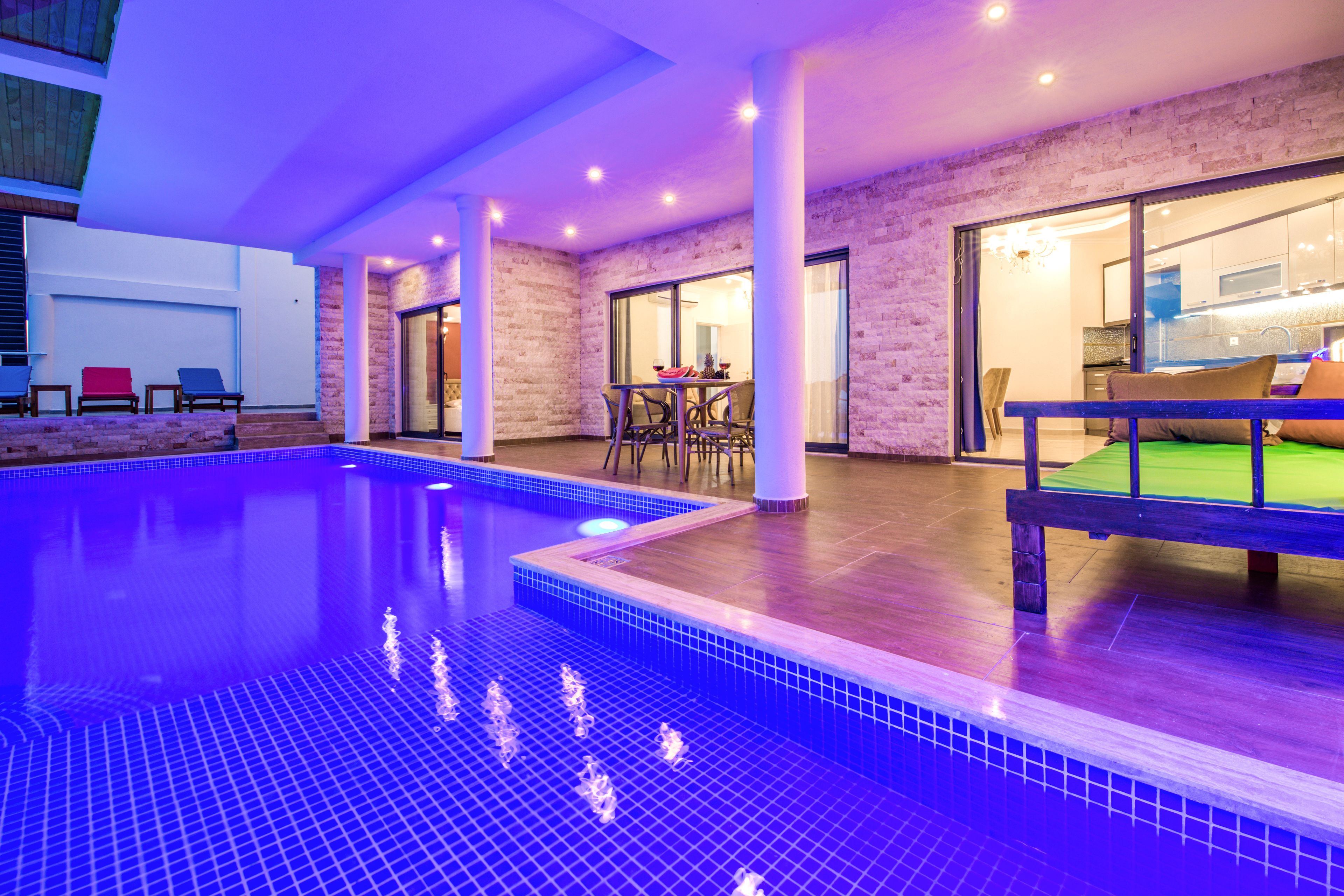 Une piscine intérieure dotée d’un sol carrelé et d’une zone de solarium en bois.