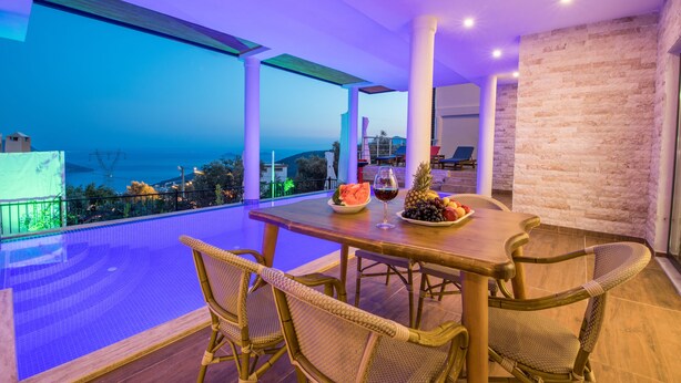 A dining area with a view of the sea, a pool, and a stone wall.