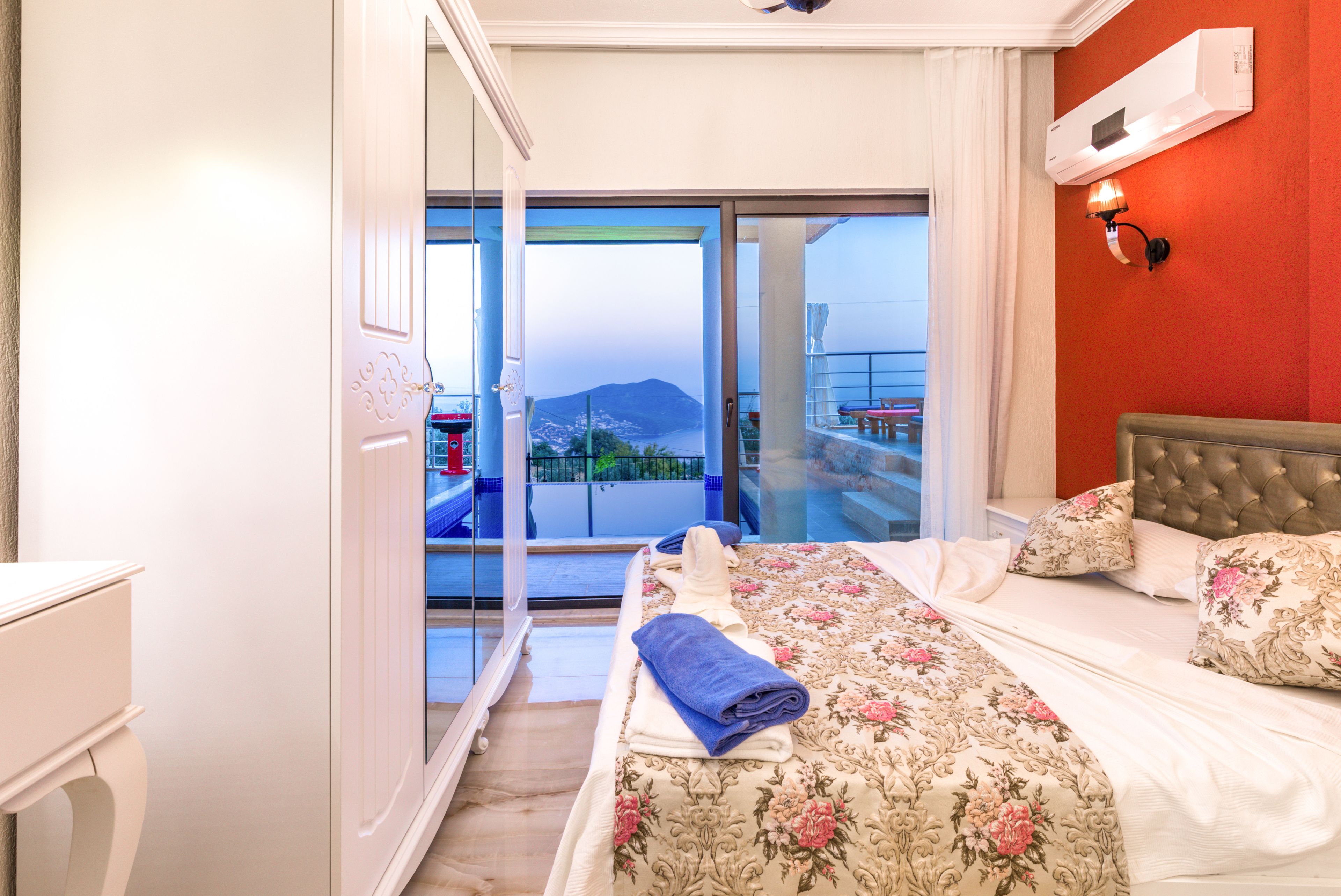 A hotel room with a bed, a bathroom, and a balcony with a view of a mountain.
