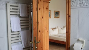 A wooden door leading to a bedroom with a bed, a toilet paper holder, and a towel rack with towels. - Pension Treenehof (Koldenbüttel)