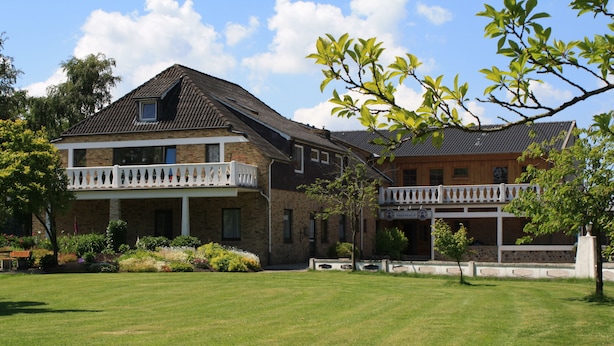 A two-story building with a balcony, a sign reading "YOUNG'S," and a well-maintained lawn. - Pension Treenehof (Koldenbüttel)