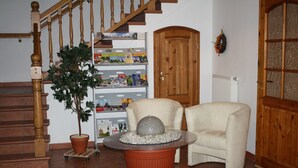 A staircase with wooden balusters, a potted plant, a round table with a decorative top, and a white armchair. - Pension Treenehof (Koldenbüttel)