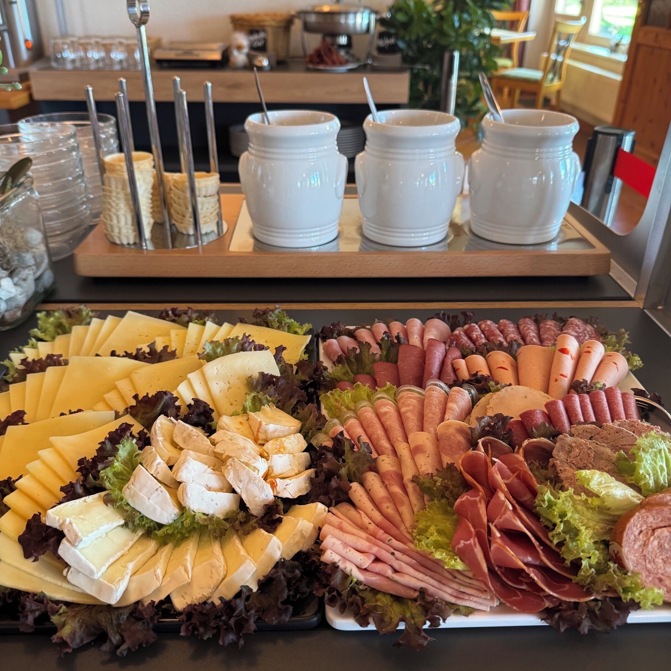 A buffet with various cheeses, meats, and vegetables.