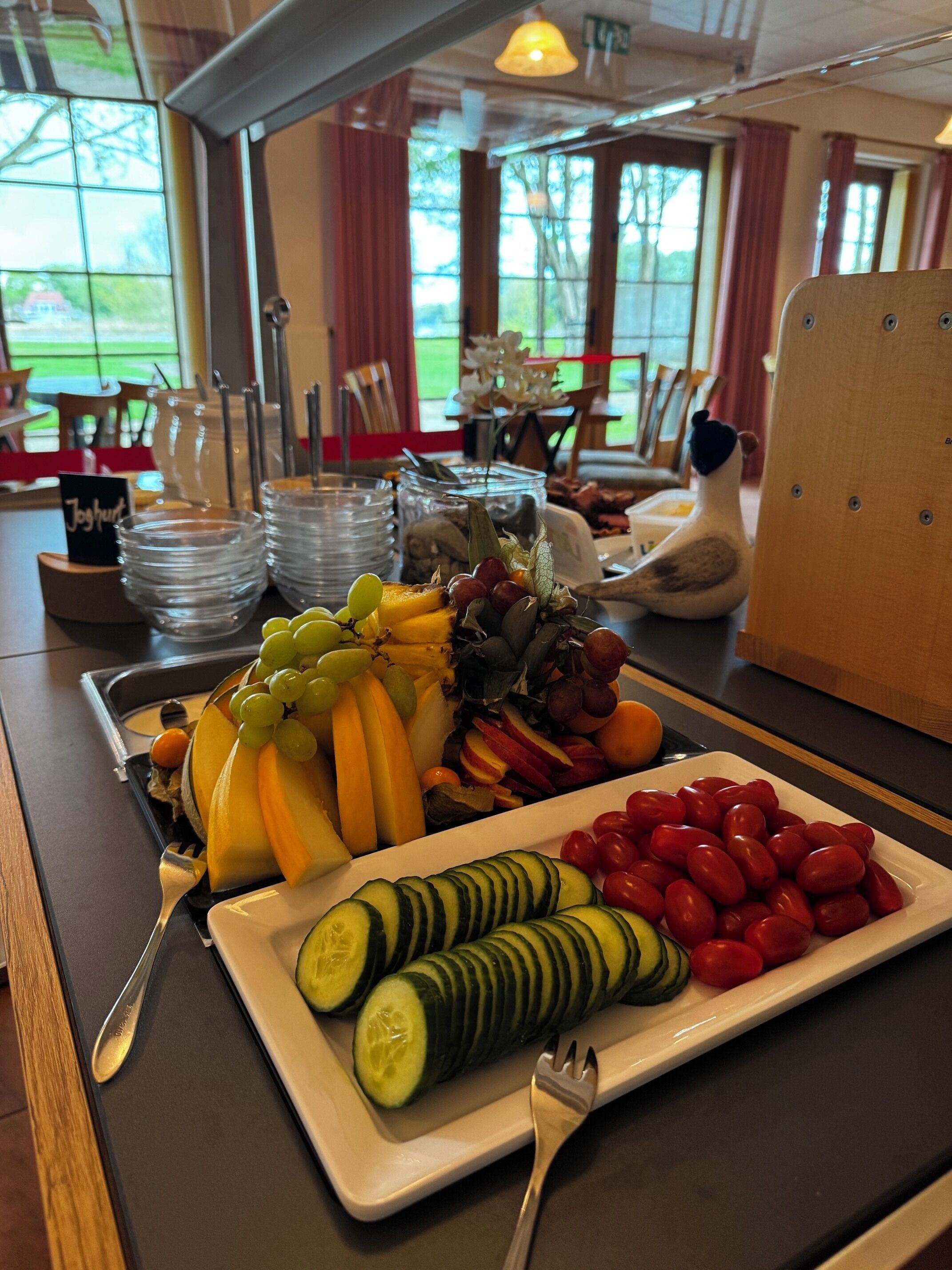 Un bufé de desayuno con diversas frutas y verduras, incluyendo pepinos en rodajas y tomates cherry, sobre una bandeja.