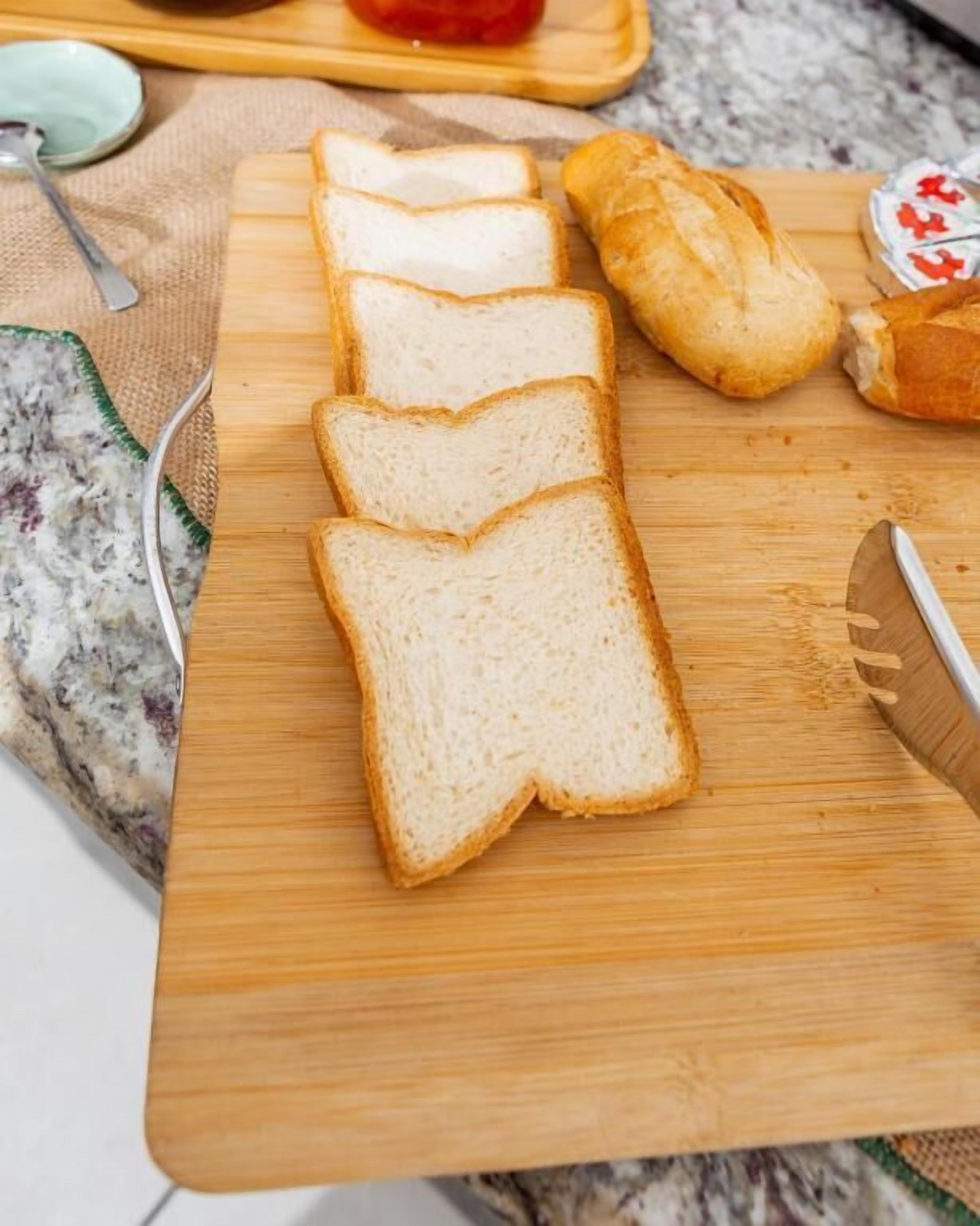 Ein Holzschnittbrett mit Weißbrot und einem Croissant auf einer Küchenarbeitsplatte.