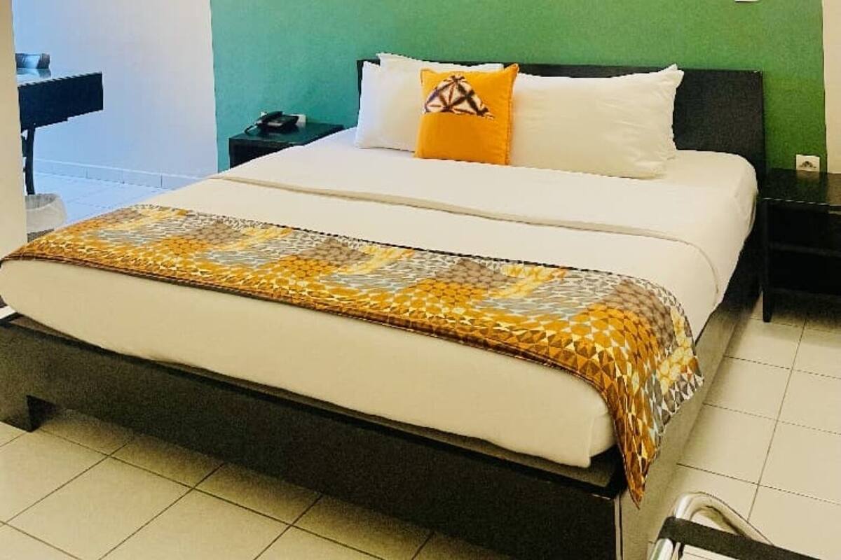 Una habitación de hotel con una cama, una mesita de noche, un aire acondicionado y una pared de acento verde.