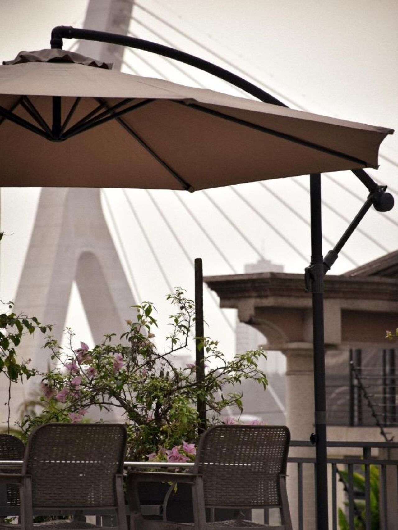 Un espace extérieur aménagé avec une table et des chaises, protégé par un grand parasol, et offrant une vue sur un pont en arrière-plan.