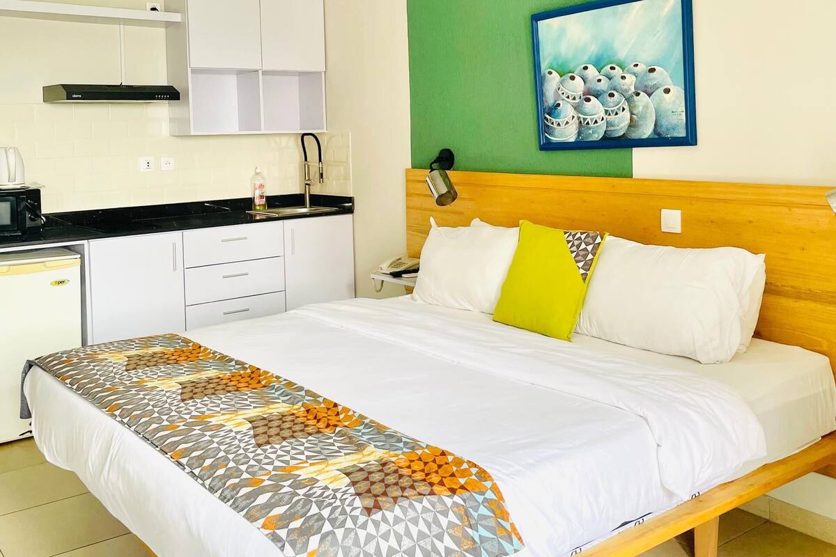 Habitación de hotel con cama, mesita de noche, escritorio, kitchenette y pared verde.