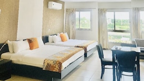 Une chambre d’hôtel avec deux lits, un bureau, des chaises, une fenêtre avec des rideaux et un luminaire au plafond.