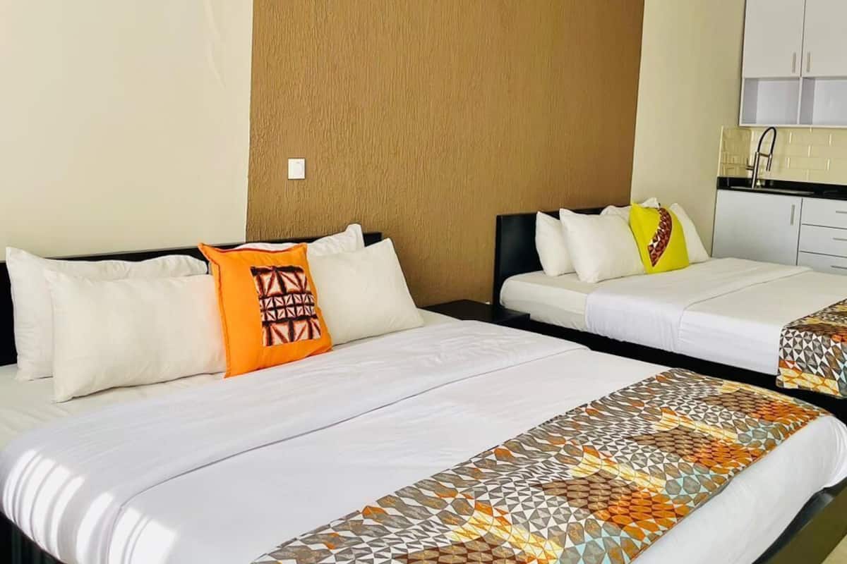 Habitación de hotel con dos camas, una pared decorativa de madera, kitchenette y unidad de aire acondicionado.
