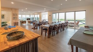 Un comedor amplio con varias mesas y sillas, una barra de madera y ventanas grandes que ofrecen vistas al exterior.