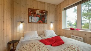 Un dormitorio con paneles de madera, una cama con ropa de cama floral, una almohada roja y un cuadro sobre la cama.
