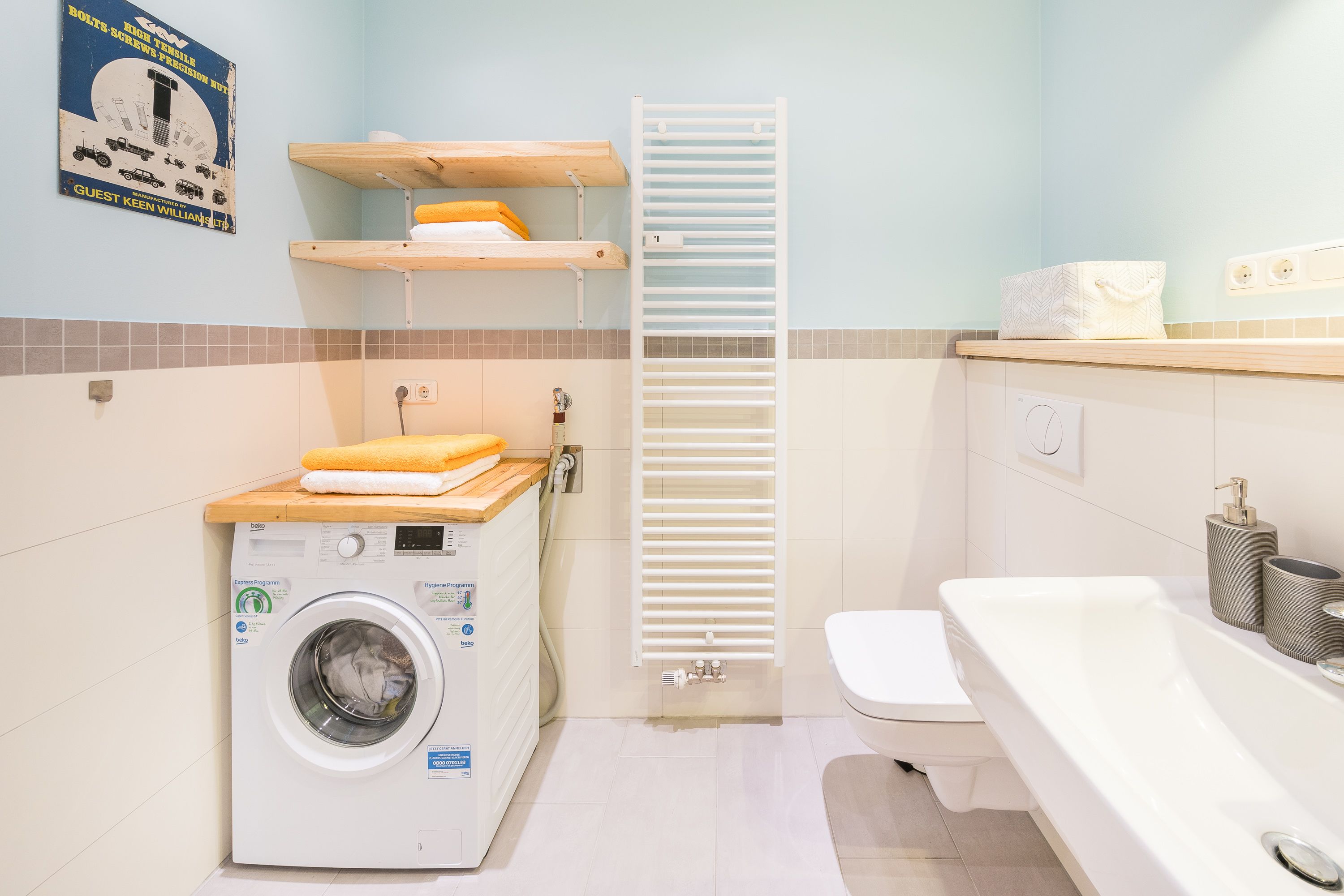 A compact hotel bathroom with a washing machine, a toilet, a bathtub, and a towel rack.