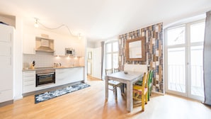 A modern kitchen with white cabinets, a microwave, and an oven. There is a dining table with chairs and a patterned rug. - Design Apartments "Potsdam West" (Potsdam)