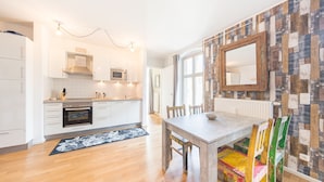 A modern kitchen with white cabinets, a wooden dining table, and colorful chairs. - Design Apartments "Potsdam West" (Potsdam)