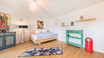 Un dormitorio con una cama de madera, una lámpara de pie, un cartel, un estante y un cubo de basura rojo.