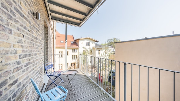 A balcony with a metal railing, a brick wall, and a view of neighboring buildings. - Design Apartments "Potsdam West" (Potsdam)
