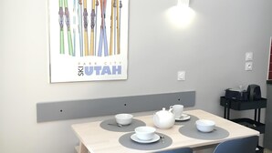 A dining area with a table set for two, a chair, a small stool, and a wall-mounted light fixture. - Val Tho, 1 bedroom, on the slopes, parking - 2 other apartments available next door  (Val Thorens)