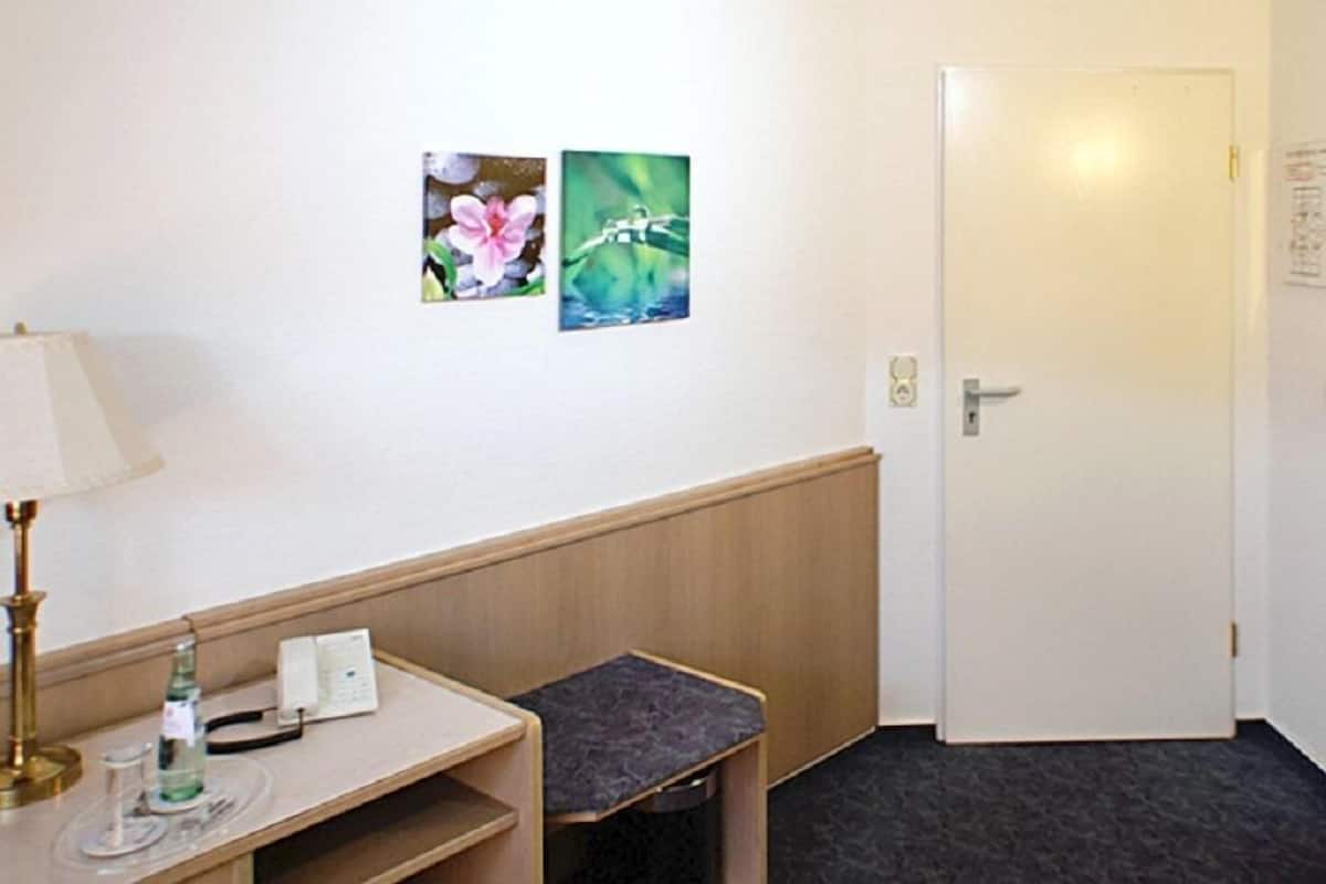 Ein Hotelzimmer mit einer hölzernen Bank, einem kleinen Tisch mit einer Lampe und zwei gerahmten Bildern an der Wand.