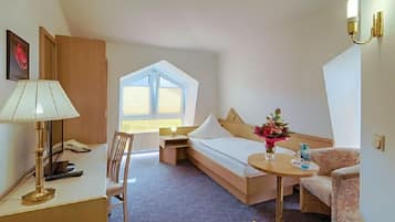 Ein Hotelzimmer mit Bett, Schreibtisch, Stuhl, einem kleinen Tisch mit Blumenvase und einem Fenster mit Jalousien.