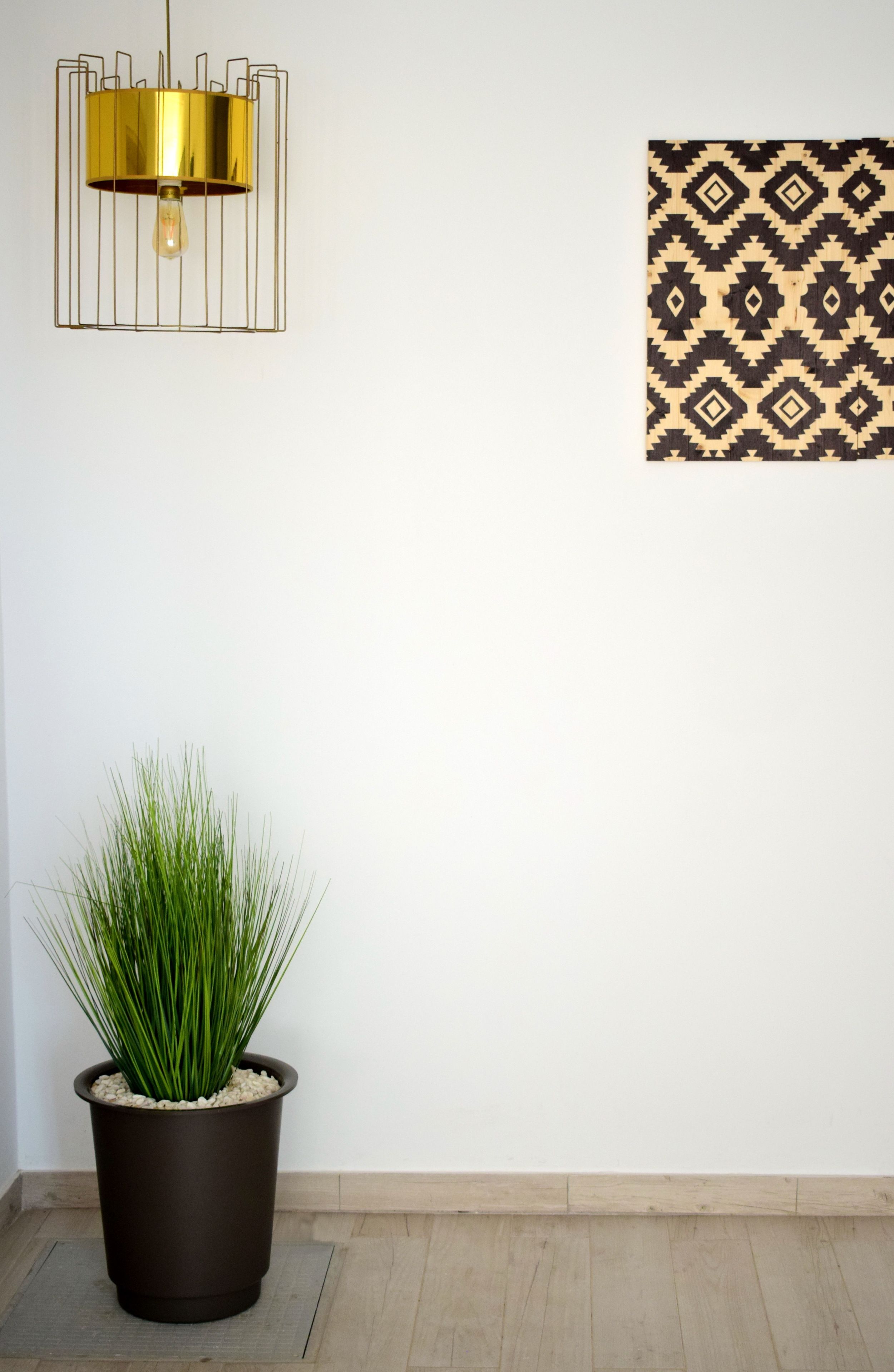 Een kamerplant in pot, een wandlamp en een wanddecoratie met een patroon.
