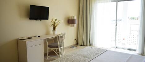 Habitación de hotel con cama, escritorio, silla, televisor, lámpara y ventana con cortinas.