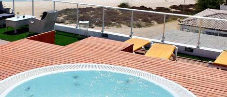 A hot tub on a wooden deck with a view of the beach and boats.