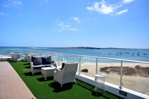 A balcony with outdoor furniture, a view of the beach, and boats in the water. - Ouril Agueda (Boa Vista)