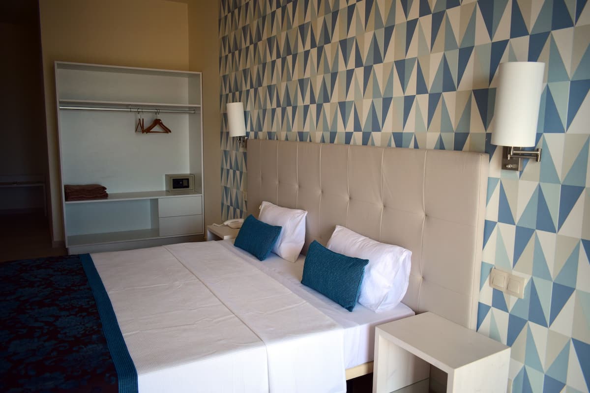 A hotel room with a large bed, a bedside table, a nightstand, a mirror, and a geometric-patterned wall.