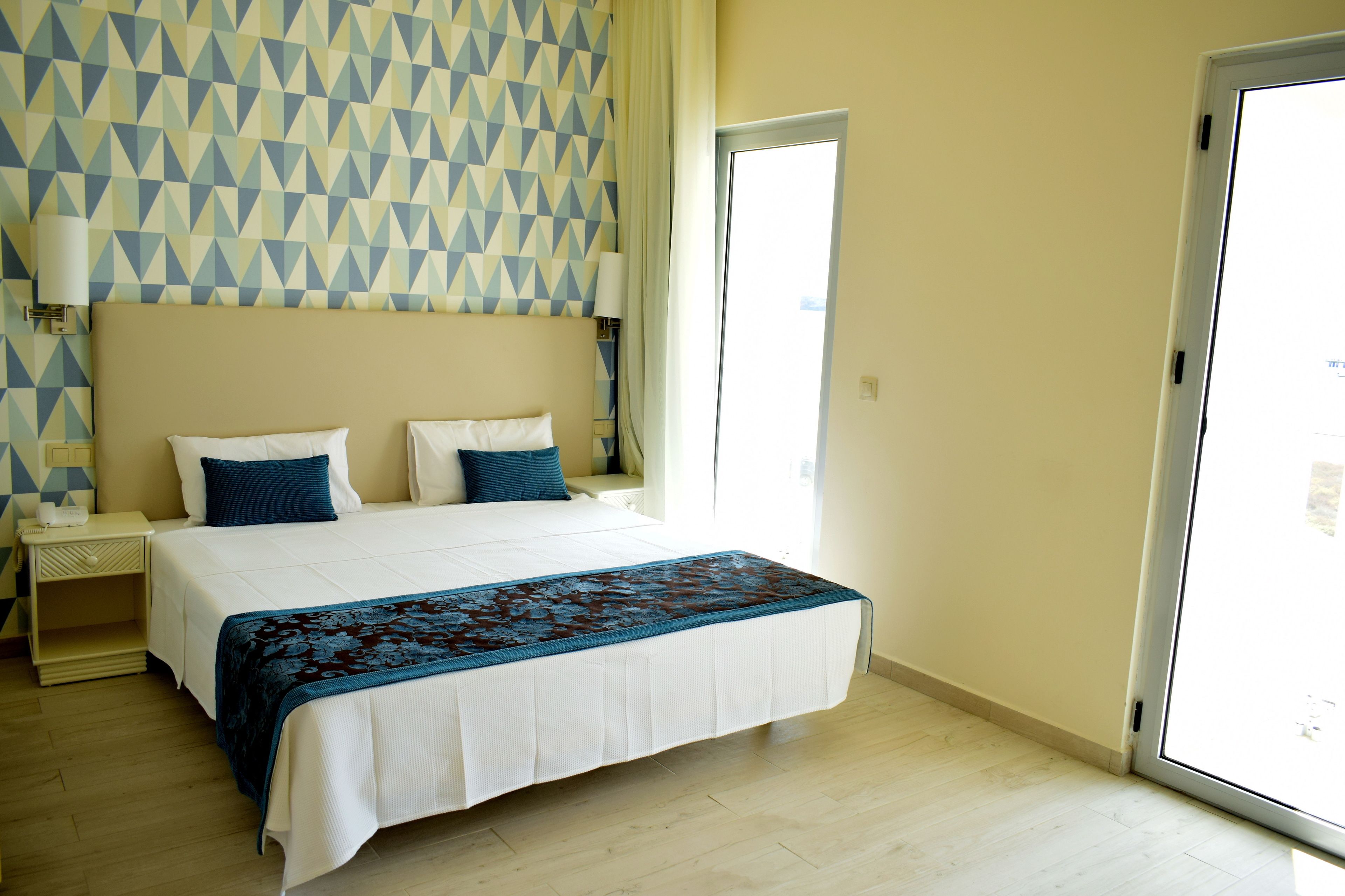 A hotel room with a large bed, a nightstand, a lamp, and a geometric-patterned wall.
