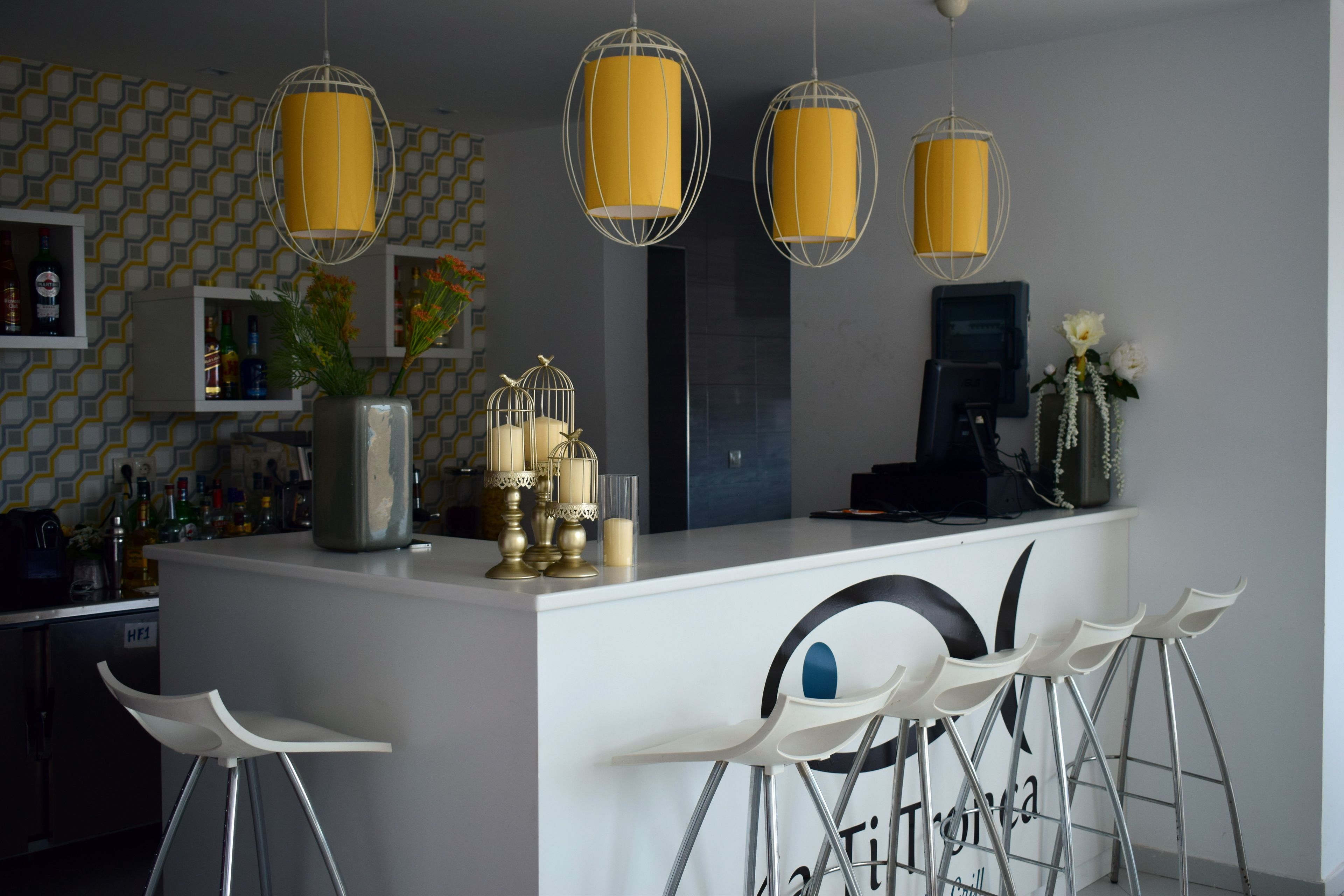 A modern kitchen with a central island, bar stools, hanging yellow pendant lights, and a patterned backsplash.