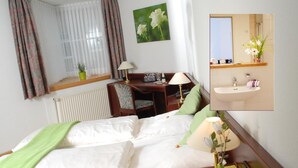 A hotel room with a bed, desk, chair, lamp, potted plant, and a bathroom with a sink and mirror. - Altstadthotel Meppen (Meppen)