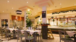 A restaurant with tables and chairs, a counter with a display case, and a large potted plant. - Altstadthotel Meppen (Meppen)