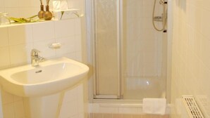 A bathroom with a sink, mirror, shower, and tiled floor. - Altstadthotel Meppen (Meppen)