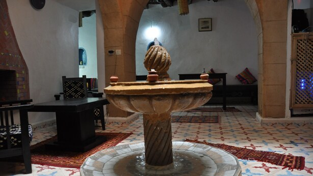A traditional fountain with a decorative top, surrounded by a tiled floor with a geometric pattern. - Apparently familial  (Ancien Médina)